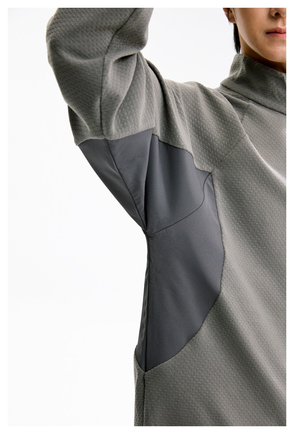 Close-up of the gray pullover's textured fabric and contrasting dark side panel beneath the raised arm.