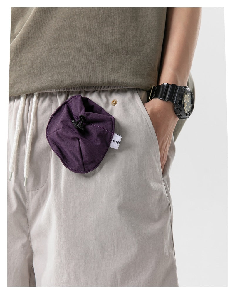 Close-up of a purple drawstring pouch attached to light gray shorts, with the model's hand in the pocket.