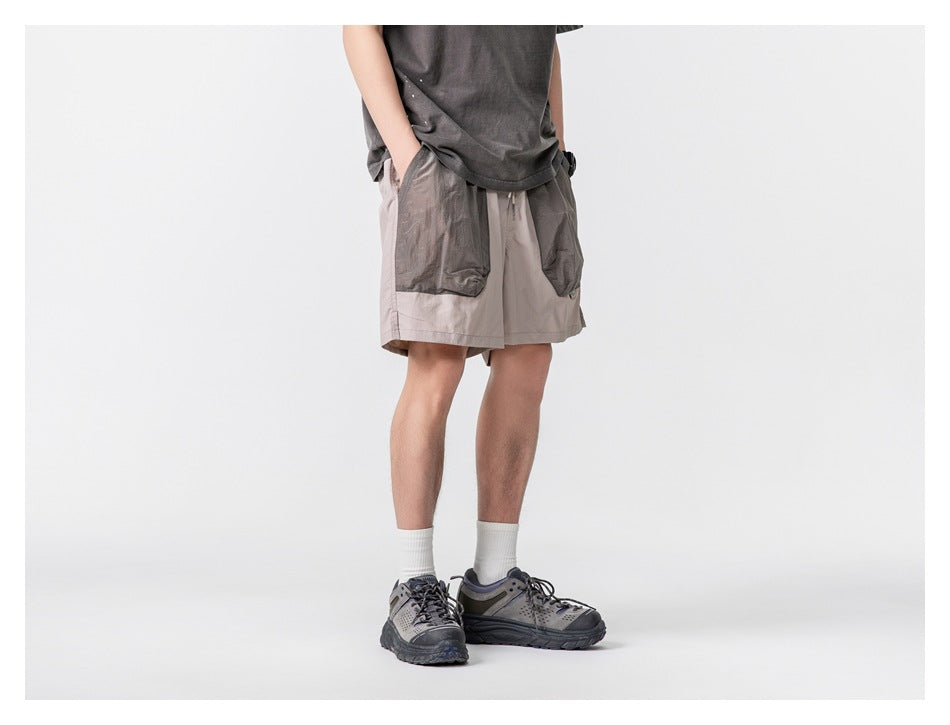 Model wearing light taupe shorts with oversized dark gray front pockets, shown at an angle.