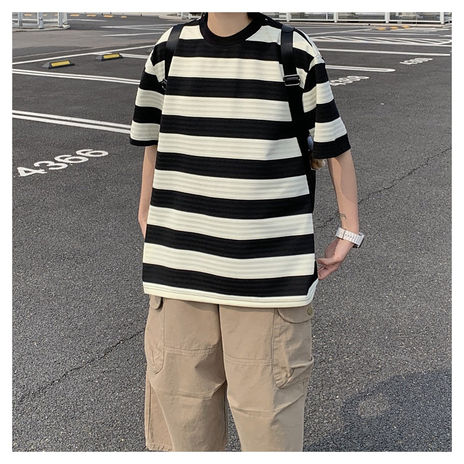 Person wearing a black and cream striped oversized T-shirt with khaki cargo shorts and a backpack in a parking lot