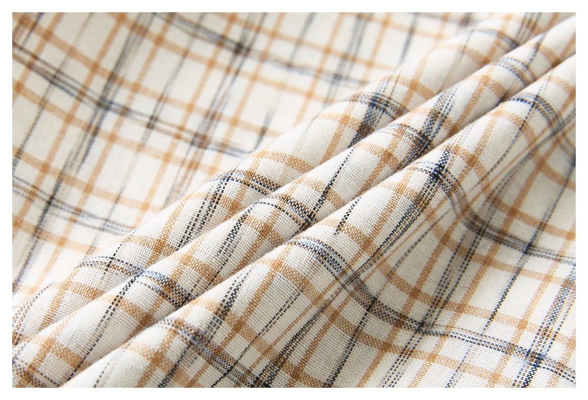 Macro view of the cream shirt fabric with intersecting tan and dark plaid lines and soft folds.