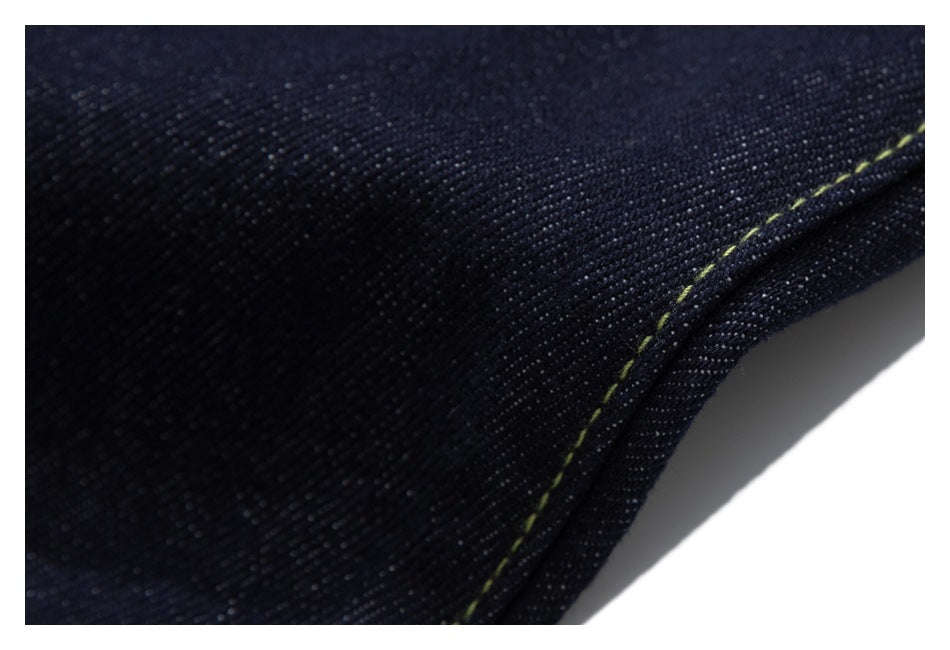 Macro view of dark indigo denim and a curved seam with contrast stitching.