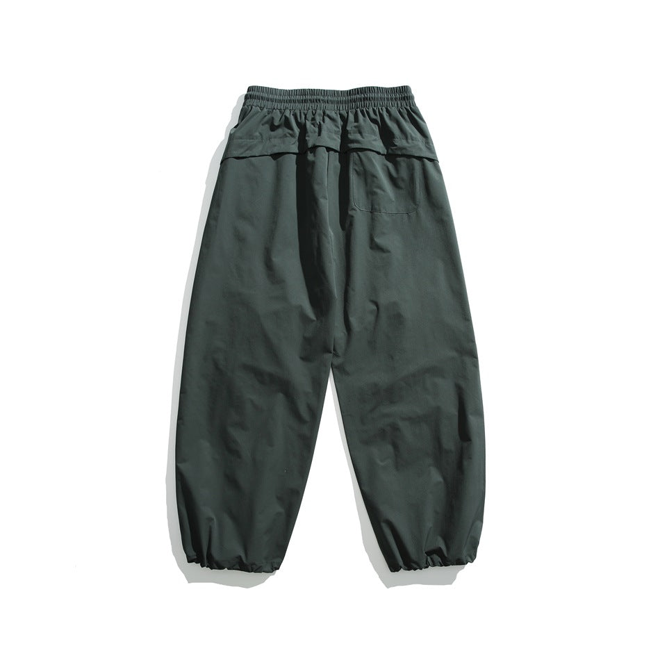 Rear view of dark teal loose trousers with an elastic waistband, one back pocket, and gathered ankle cuffs.