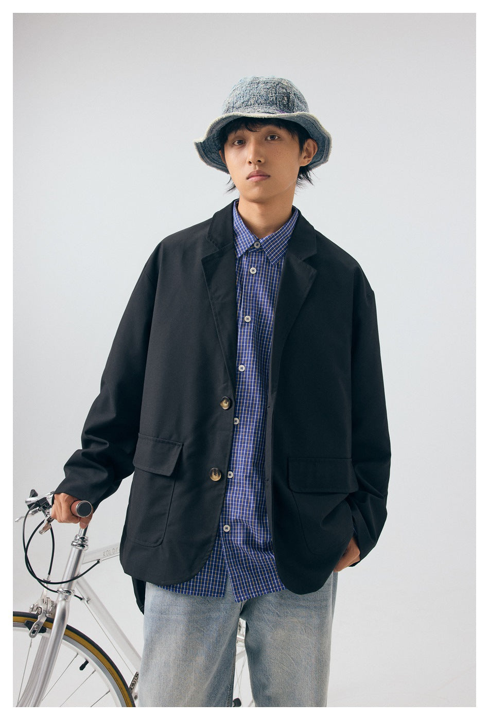 Front view of a person wearing an oversized black blazer with flap pockets over a blue checked shirt.
