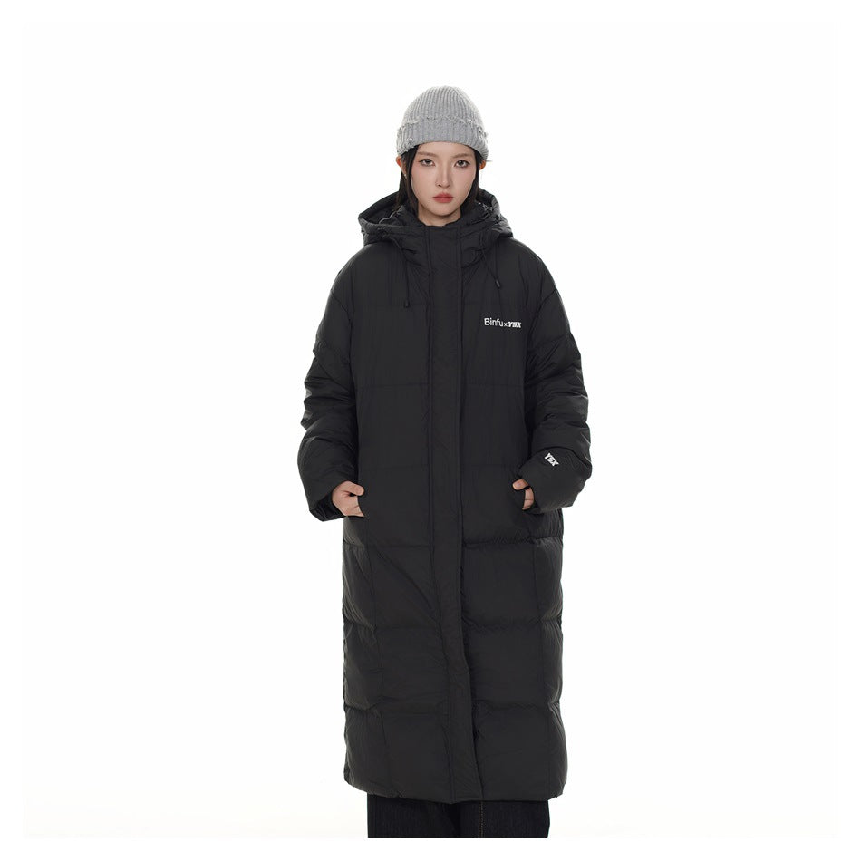 Front view of a model wearing a long black hooded puffer coat and gray knit beanie.
