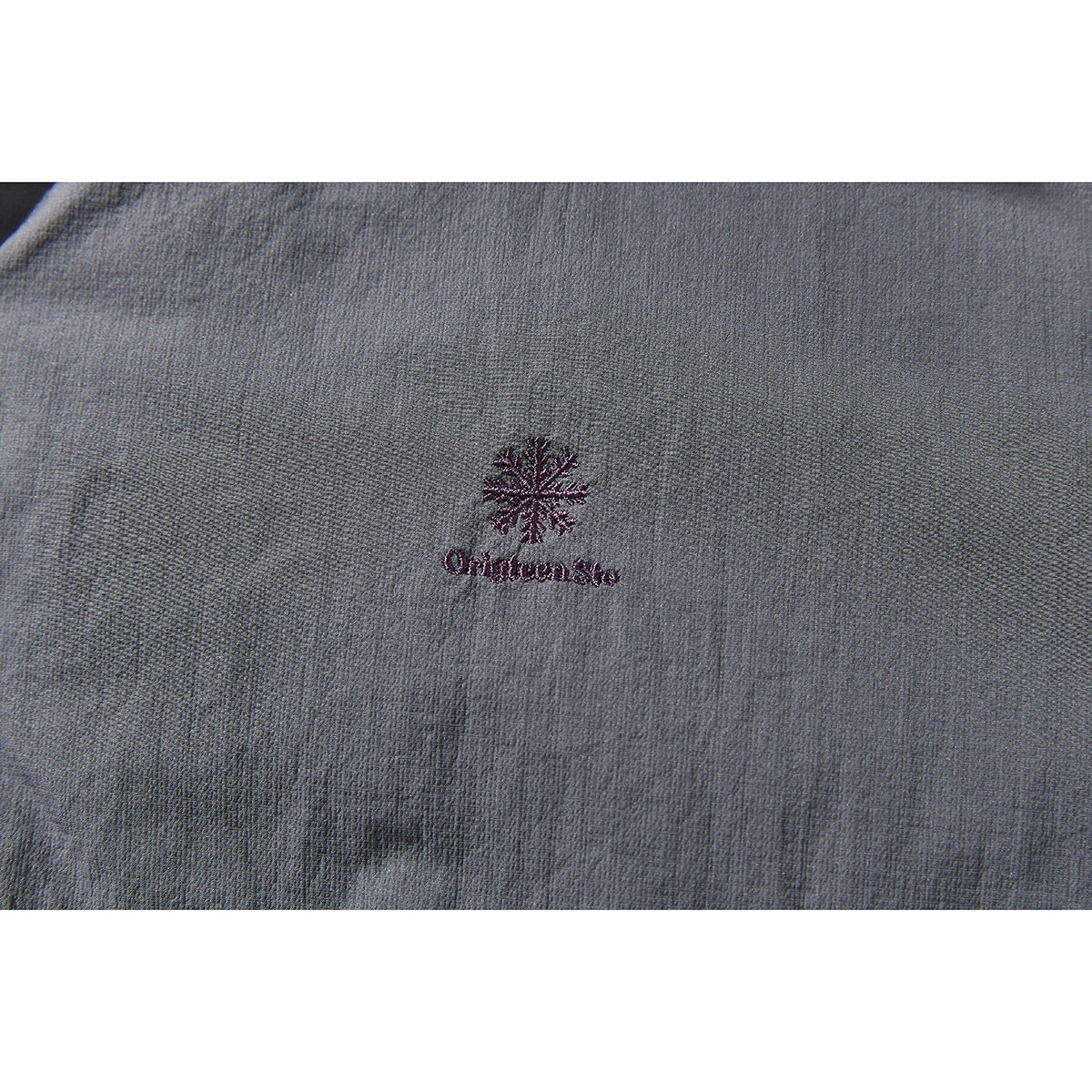 Close-up of a small plum embroidered emblem and lettering on gray jacket fabric.