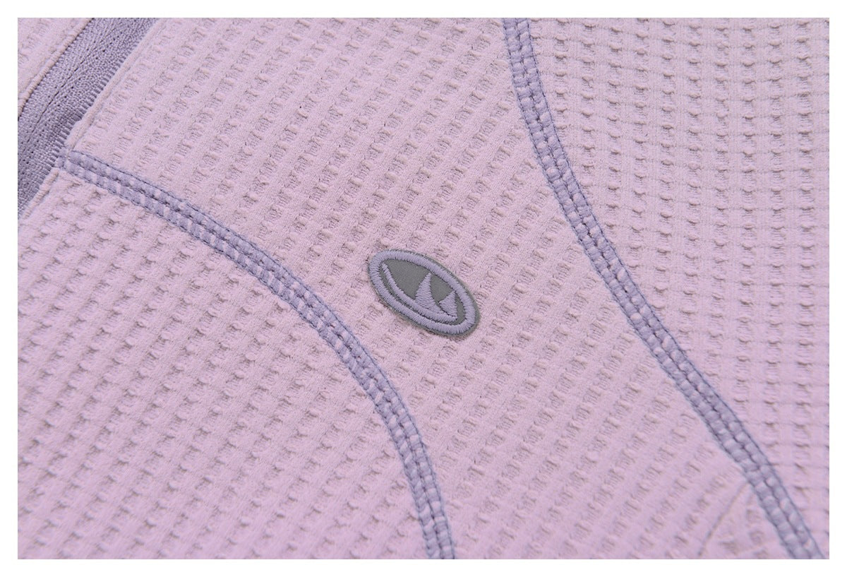 Close-up of an embroidered oval emblem and gray seam stitching on mauve textured fabric.
