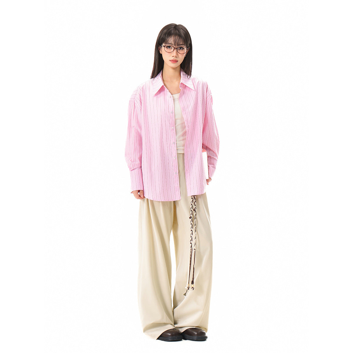 Model wearing an oversized pink pinstriped button-up shirt over a light top and cream trousers.