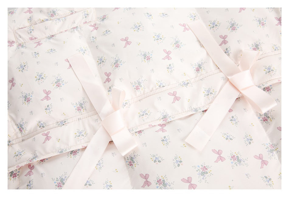 Close-up of a pale pink floral-and-bow print garment with wide ribbon ties crossing over its piped edge.