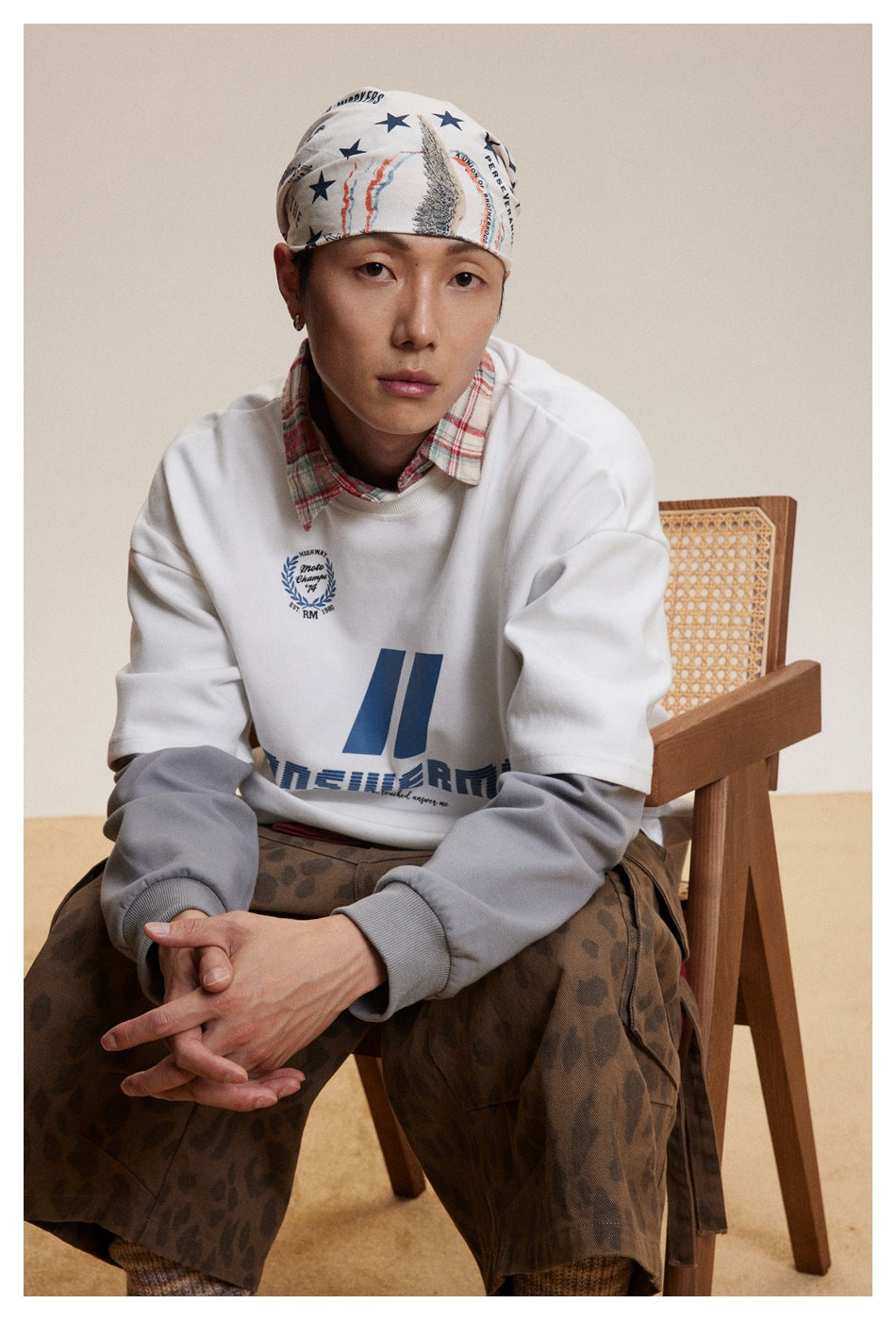 Model wearing a white sweatshirt with gray sleeves and blue graphics, styled with a printed headscarf and brown patterned