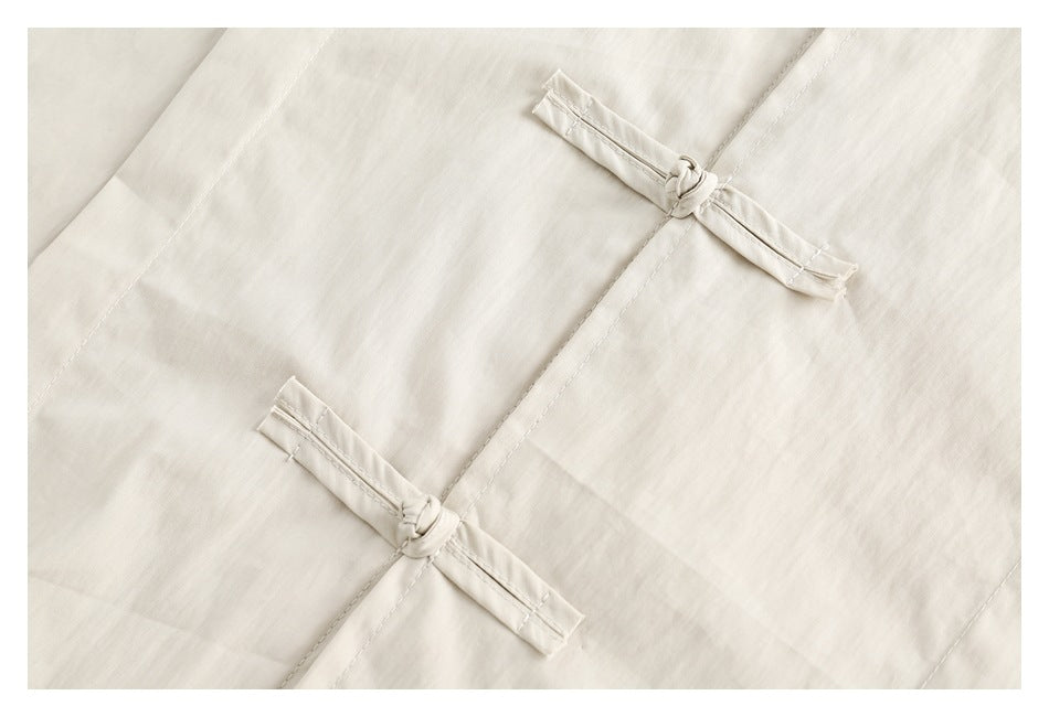 Close-up of an ivory garment panel with two fabric frog closures and visible stitching.