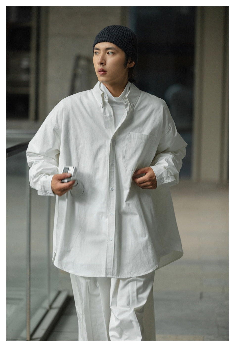 Model wearing an oversized white button-up shirt with a chest pocket and white trousers.