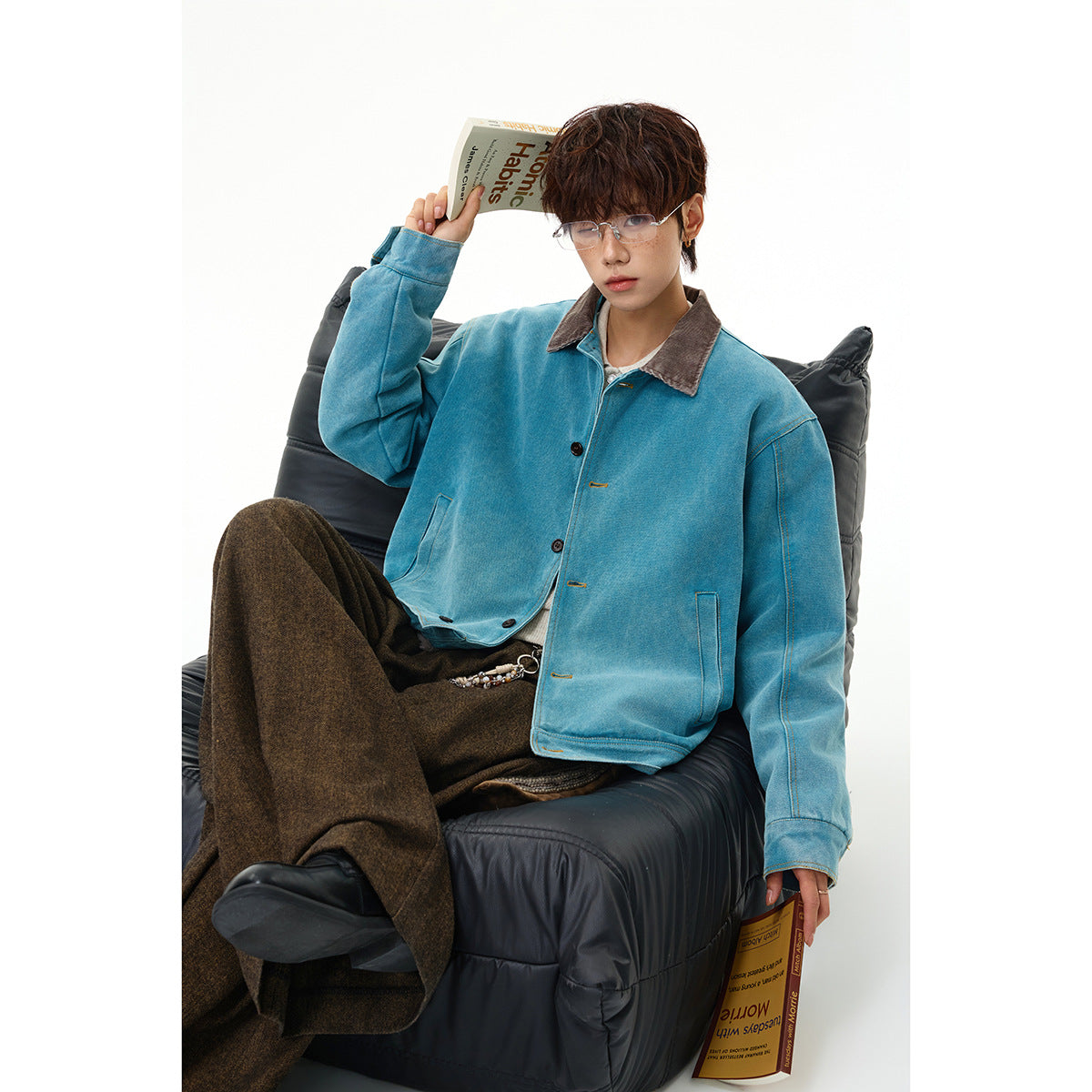 Model seated in a bright teal button-front jacket with a brown collar and dark wide-leg trousers.