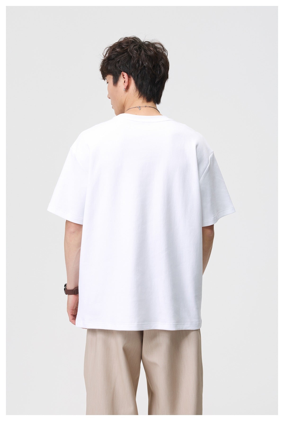 Back view of a model wearing a plain white oversized short-sleeve crew-neck tee with beige trousers.