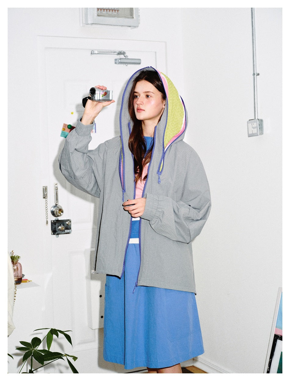 Three-quarter view of a model wearing a gray hooded jacket with colorful lining over a blue dress.