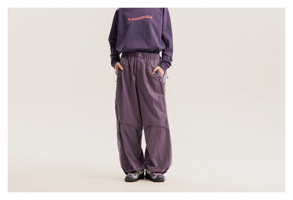 Model wearing loose plum-purple pants with an elastic waist and curved knee panels, shown from the front.