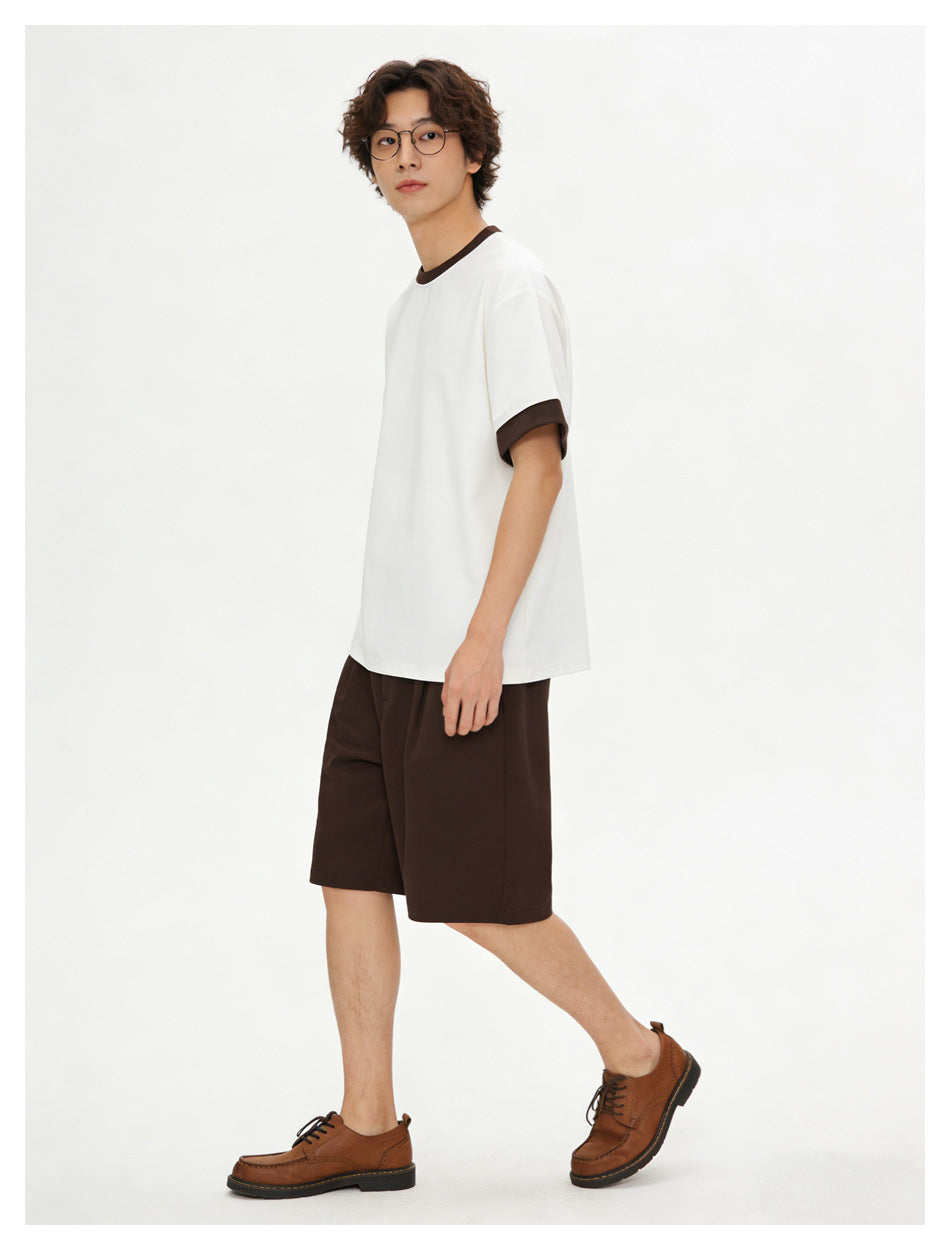 Model wearing a white T-shirt with dark brown trim and dark brown shorts, shown in a three-quarter side pose.