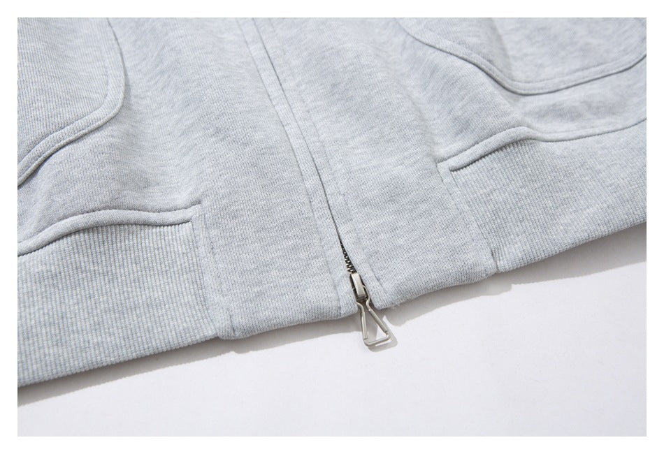 Close-up of a light gray heather zip-up sweatshirt front, showing the metal zipper and curved pocket seams.
