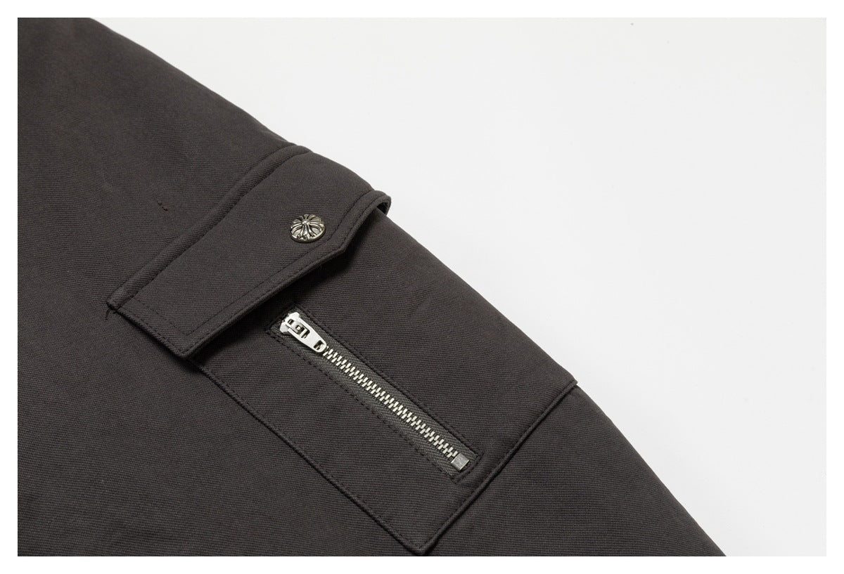 Close-up of a charcoal garment with a silver zipper pocket and decorative button tab.