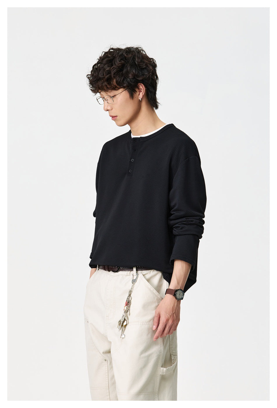Model wearing a black ribbed long-sleeve henley with cream trousers, shown from the front at an angle.