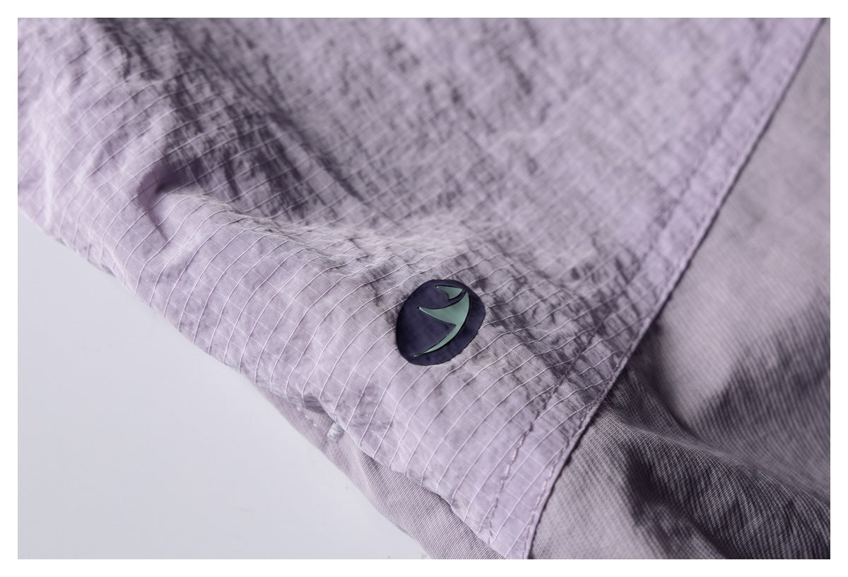 Close-up of a dark circular emblem on a lavender-gray garment with a subtle grid pattern.