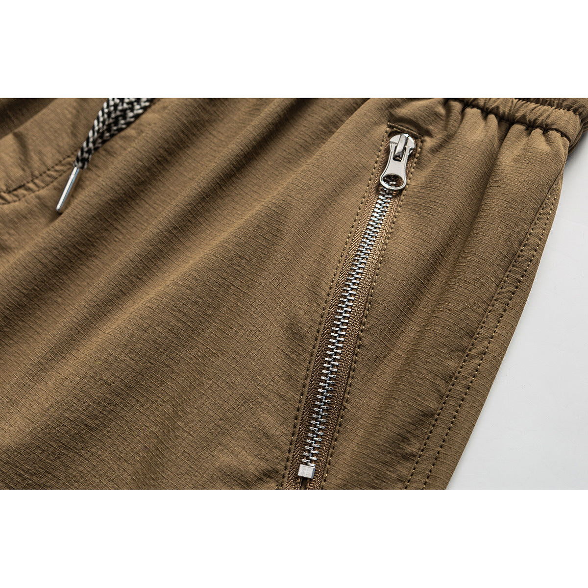 Close-up of brown shorts showing a silver side zipper, textured fabric, and part of a braided drawstring.