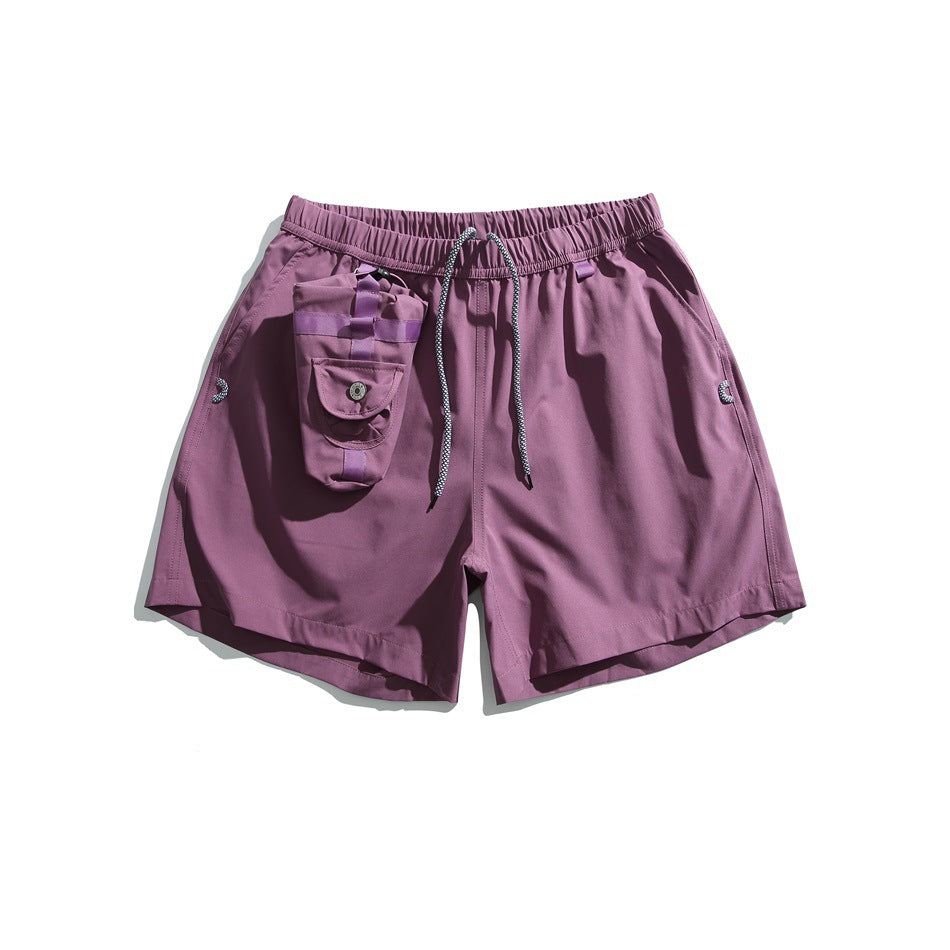 Front view of plum-purple shorts with an elastic drawstring waist, side pockets, and a small attached utility pouch.
