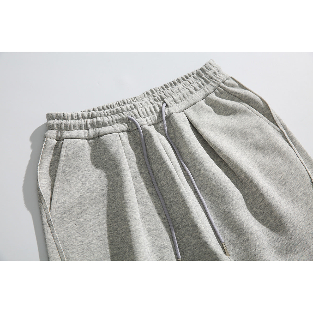 Close-up of heather-gray sweatpants showing the elastic waistband, front pockets, and long drawstrings.