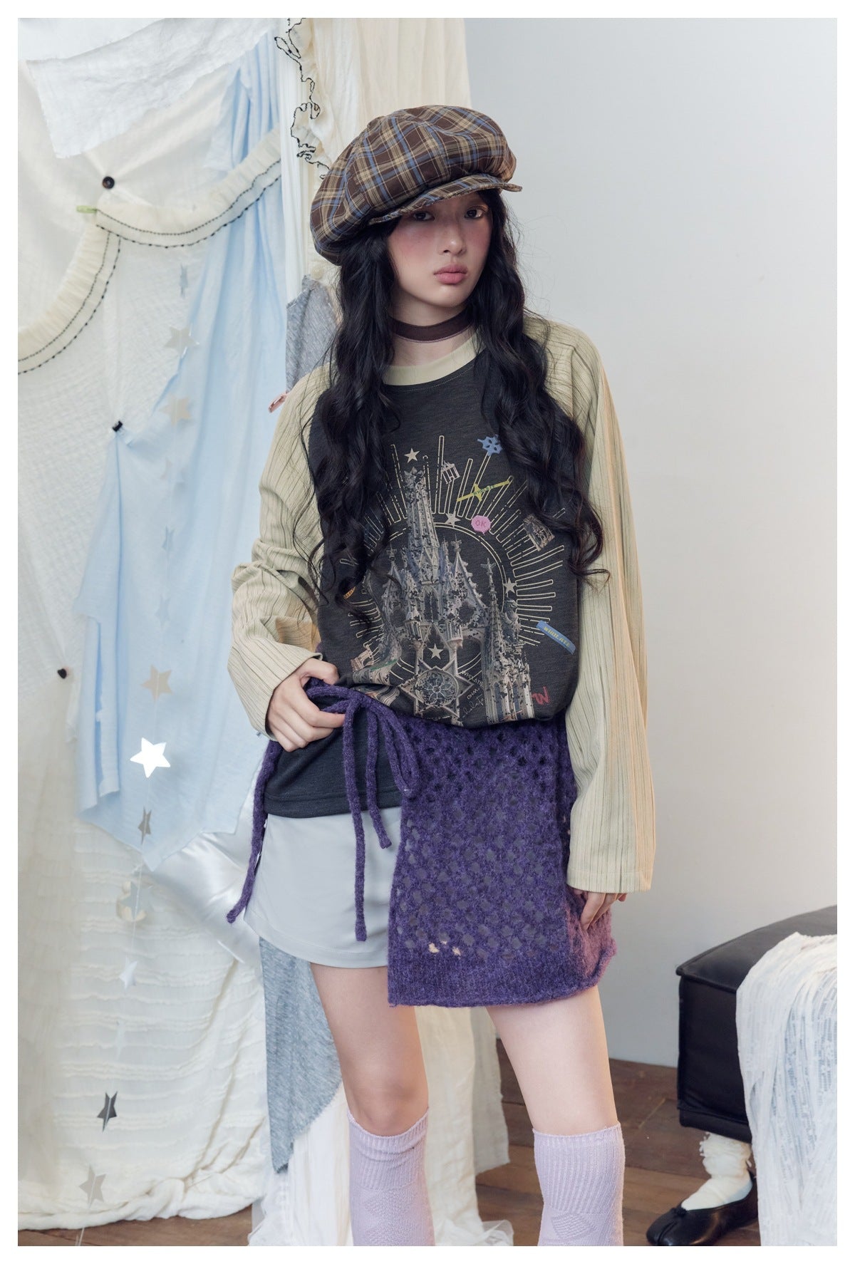 Model wearing a charcoal castle-print raglan top with cream striped sleeves and a purple knit wrap over pale shorts.