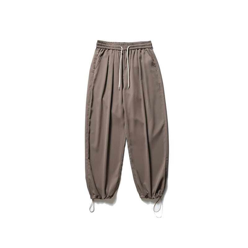 Taupe jogger pants with a drawstring elastic waist and gathered cuffs with dangling cords.