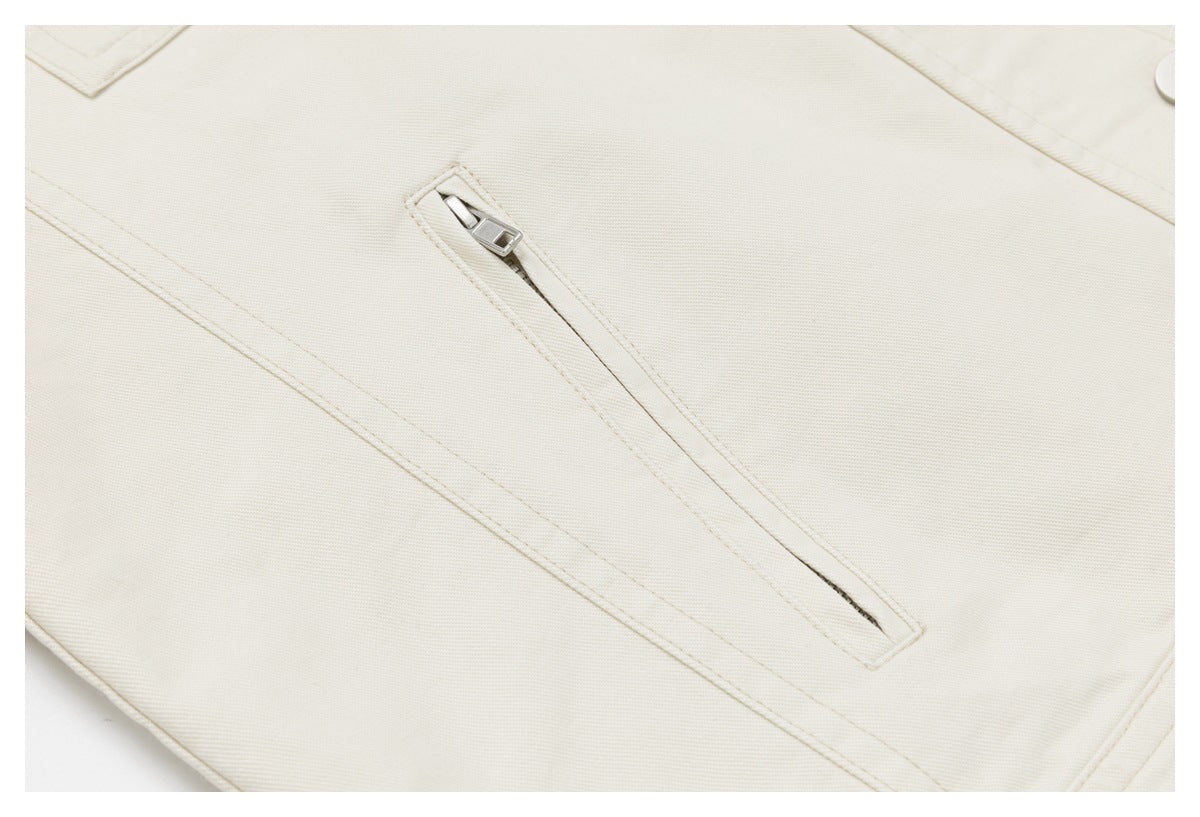 Close-up of an ivory garment showing a diagonal zippered pocket and neat stitching.