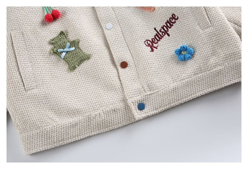 Close-up of the jacket hem with textured fabric, colorful buttons, appliqués, and embroidered lettering.