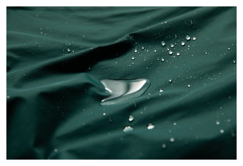 Water droplets bead on dark teal garment fabric in a close-up view.