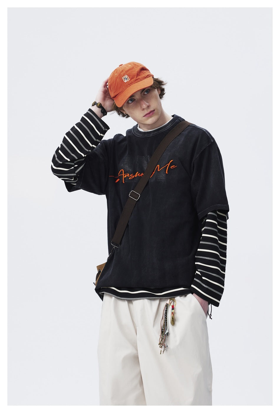 Model wearing a black graphic T-shirt over black-and-white striped sleeves and loose white pants, posing with one hand near