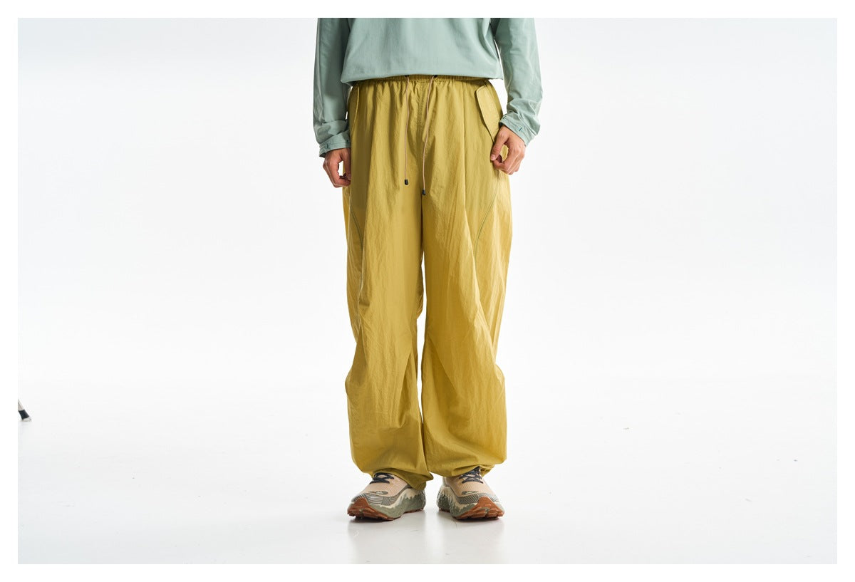 Cropped front view of a model wearing loose mustard-yellow trousers with an elastic waist and drawstring.