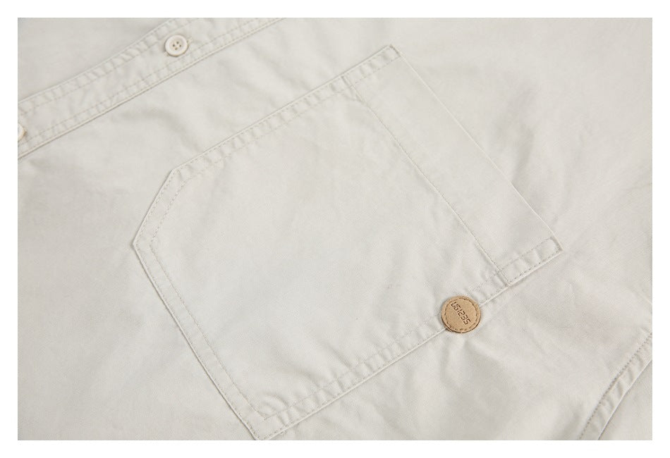 Close-up of an off-white shirt's chest pocket, stitching, and small tan button.