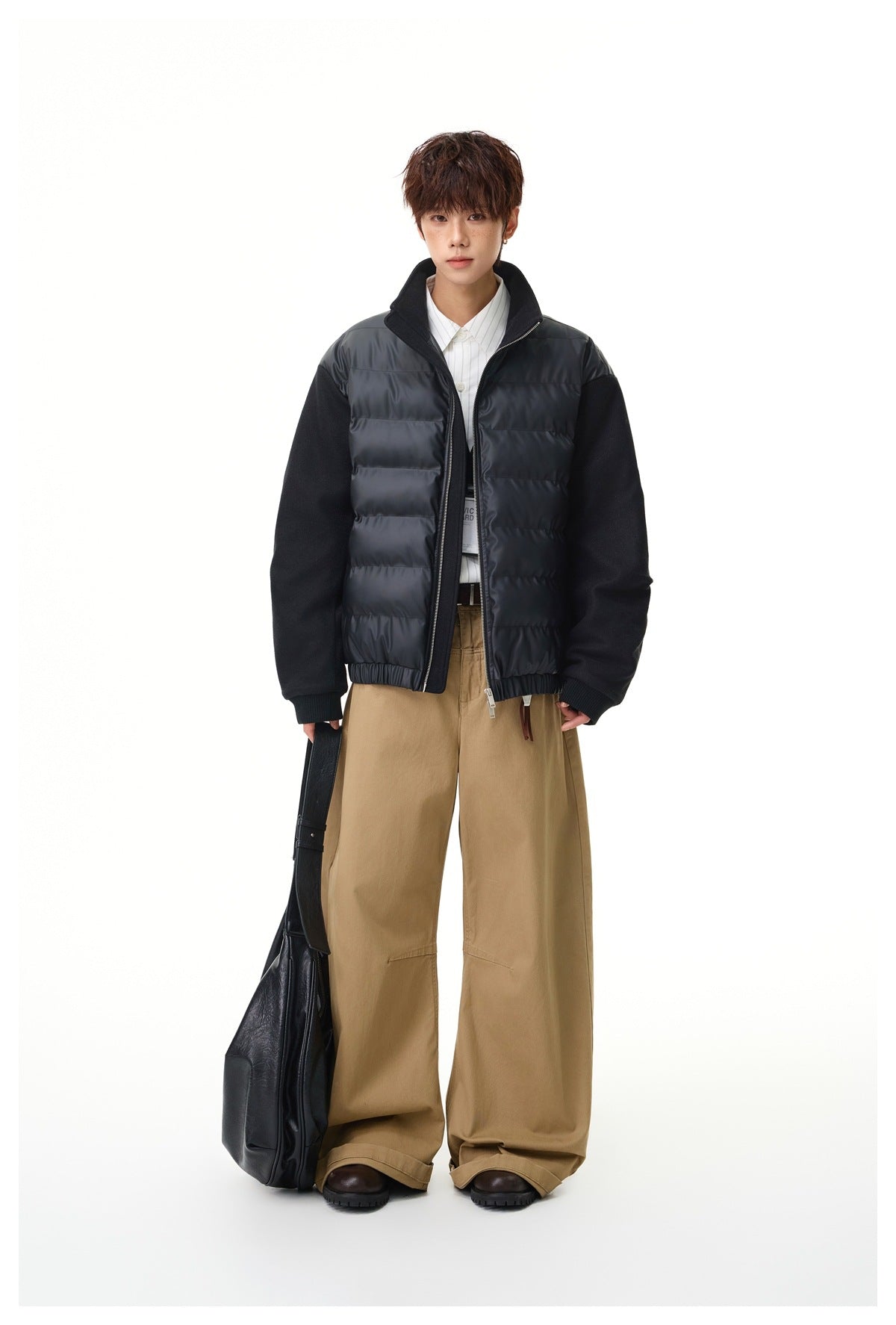 Model wearing a black quilted zip jacket with black sleeves and a raised collar, paired with tan trousers.