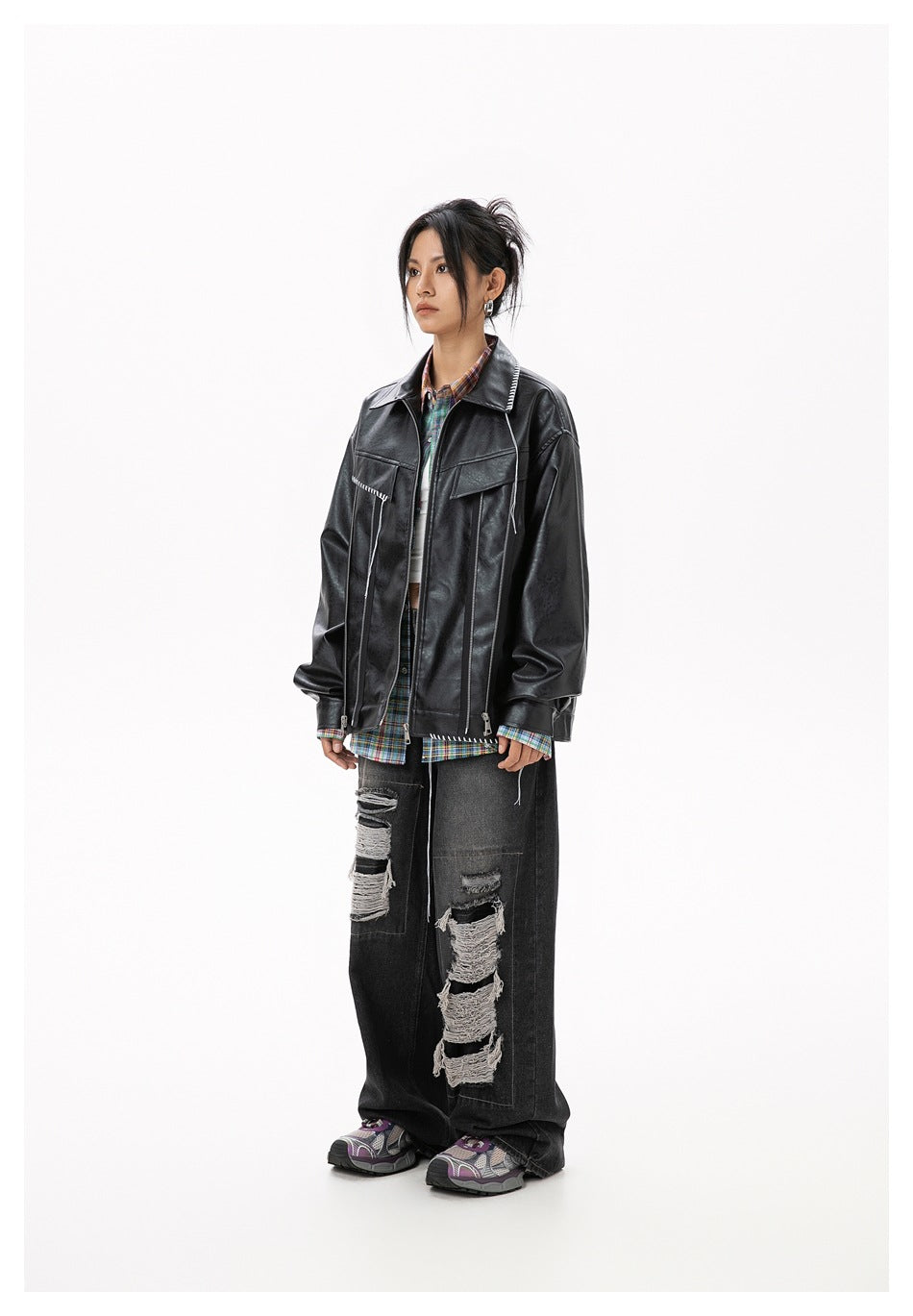 Model wearing a black leather-look zip jacket over a plaid shirt with ripped wide-leg jeans, side view
