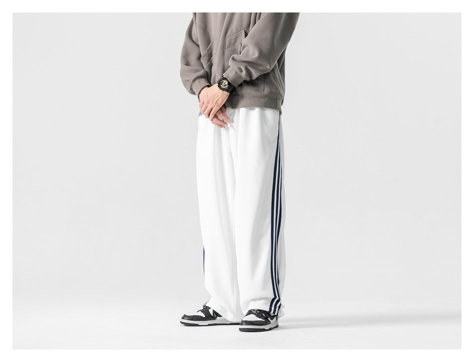 Model in white wide-leg striped pants with gray top and sneakers, cropped three-quarter side view