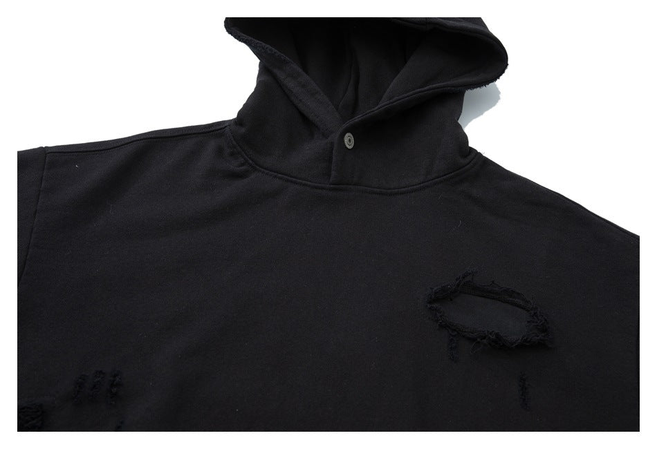 Upper-front close-up of a black hooded pullover with a snap at the neck and distressed patches.