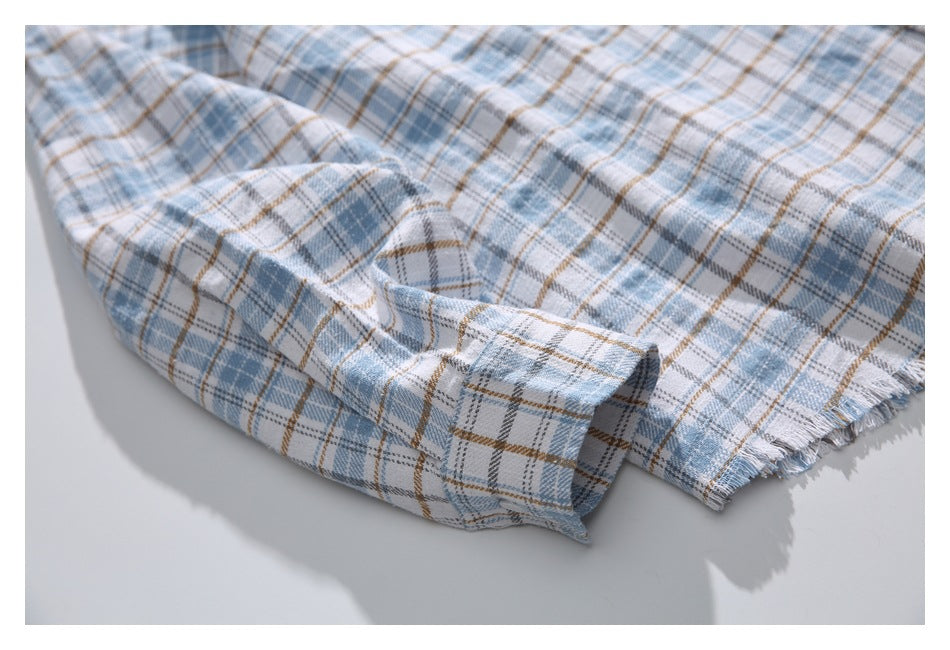 Close-up of a plaid shirt sleeve cuff and frayed edge in light blue, gray, white, and tan.