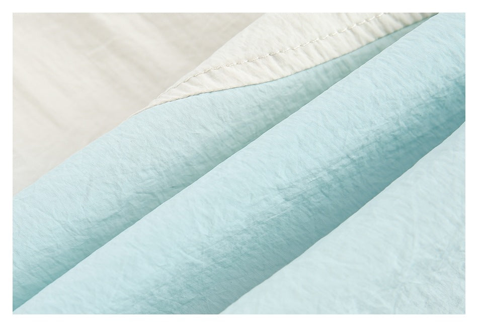 Close-up of layered pale blue and ivory bedding fabric and stitching.