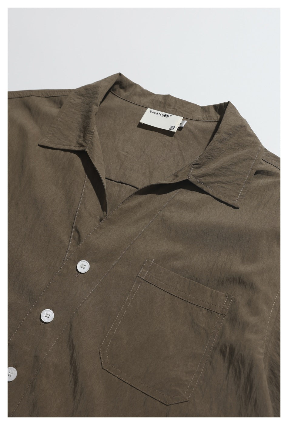 Close-up of a brown short-sleeve shirt showing its collar, white buttons, chest pocket, and neck label.