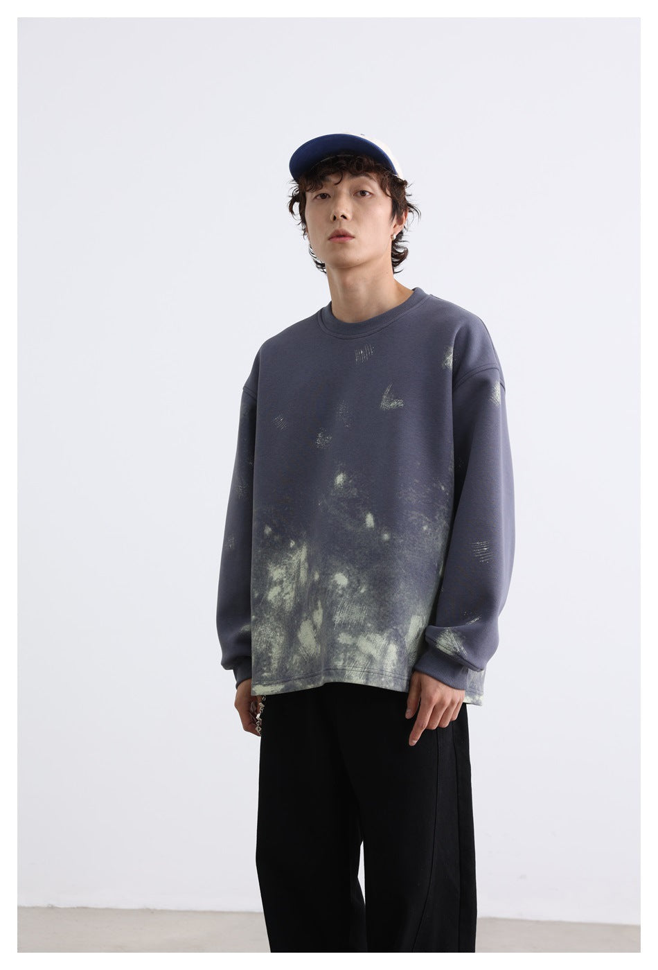 Model wearing a slate-blue oversized crewneck sweatshirt with pale distressed graphics, shown from the front.