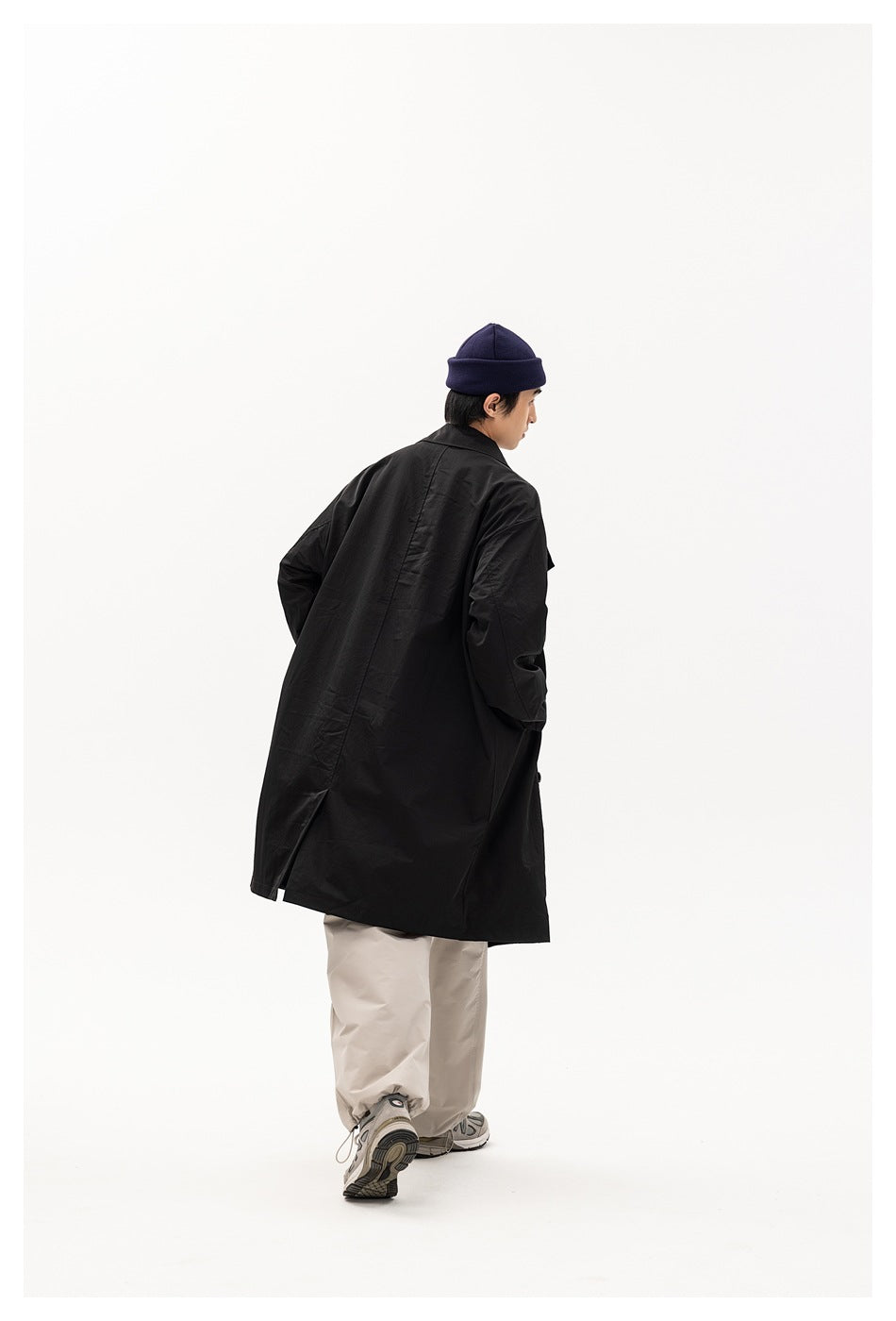 Rear view of a model wearing a long black coat with a center seam and back hem vent.