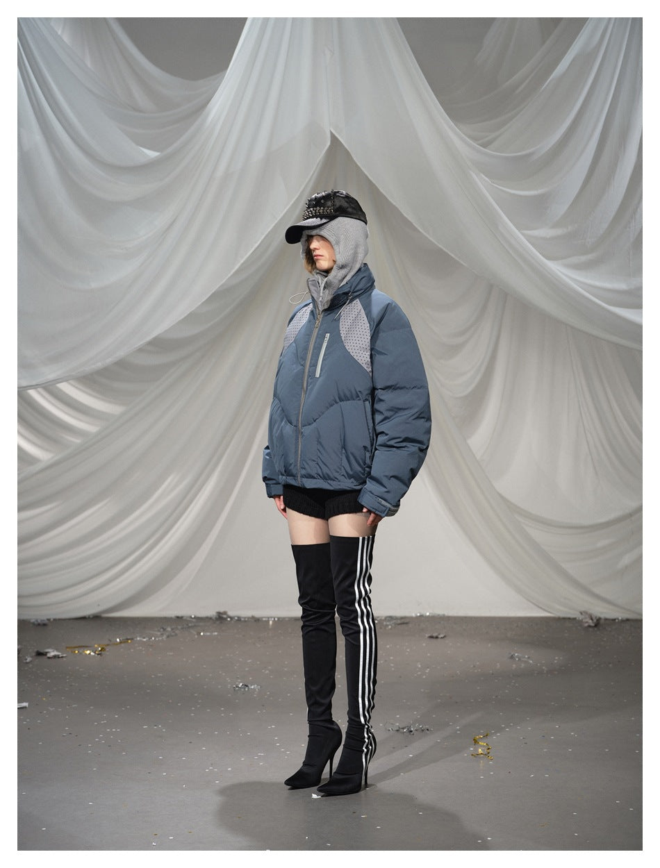 Model wearing a blue-gray zip-up puffer jacket with dotted shoulder panels, styled with black shorts and thigh-high boots.