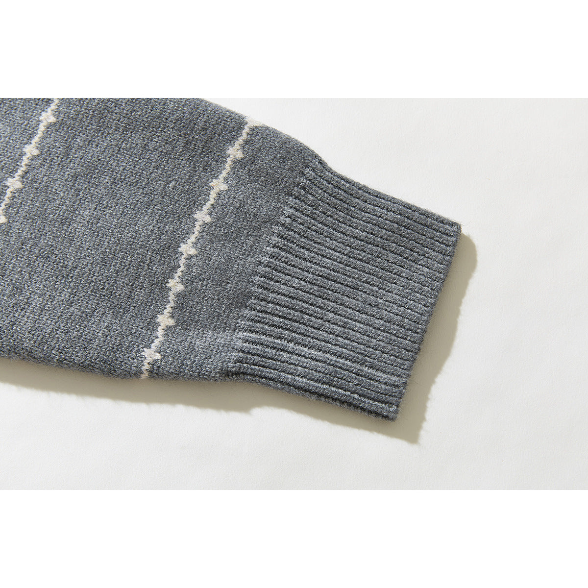 Close-up of a gray knit sweater sleeve ending in a ribbed cuff, with a cream stripe.