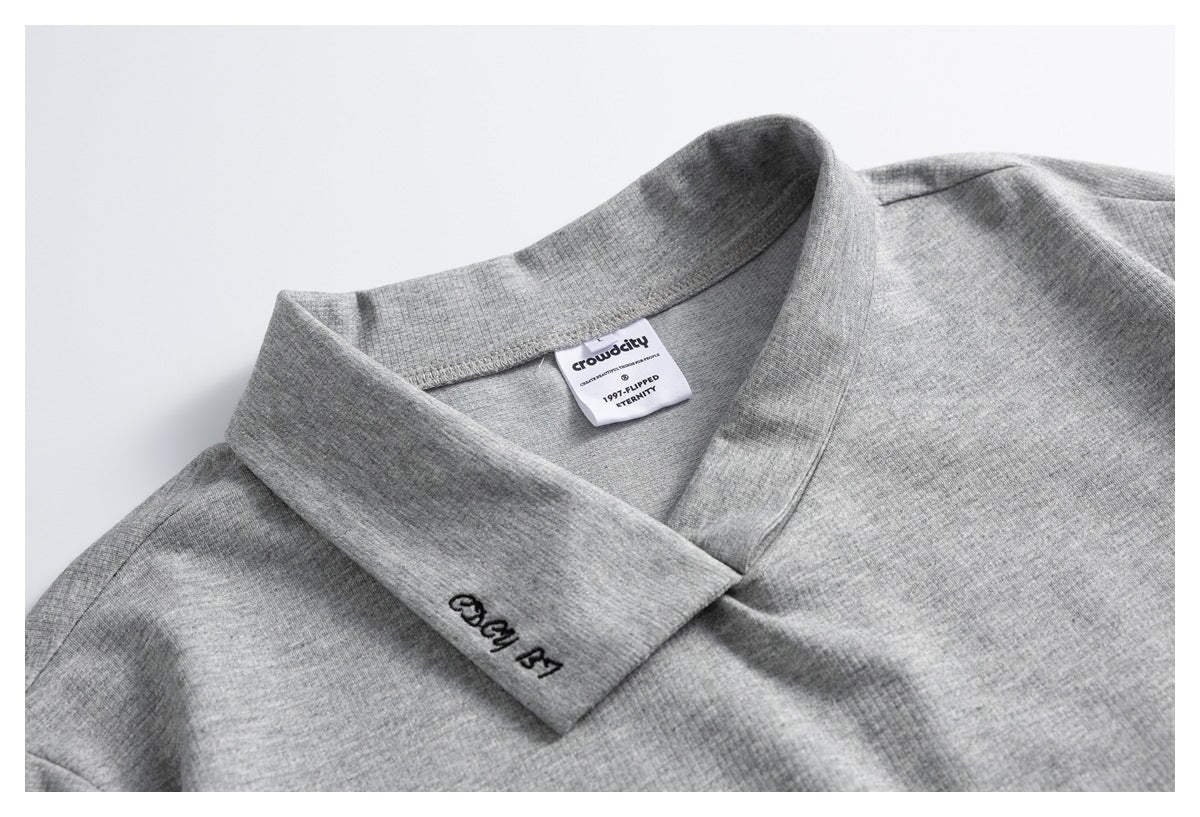 Close-up of a heather-gray crossover collar with a sewn neck label and small black embroidery.