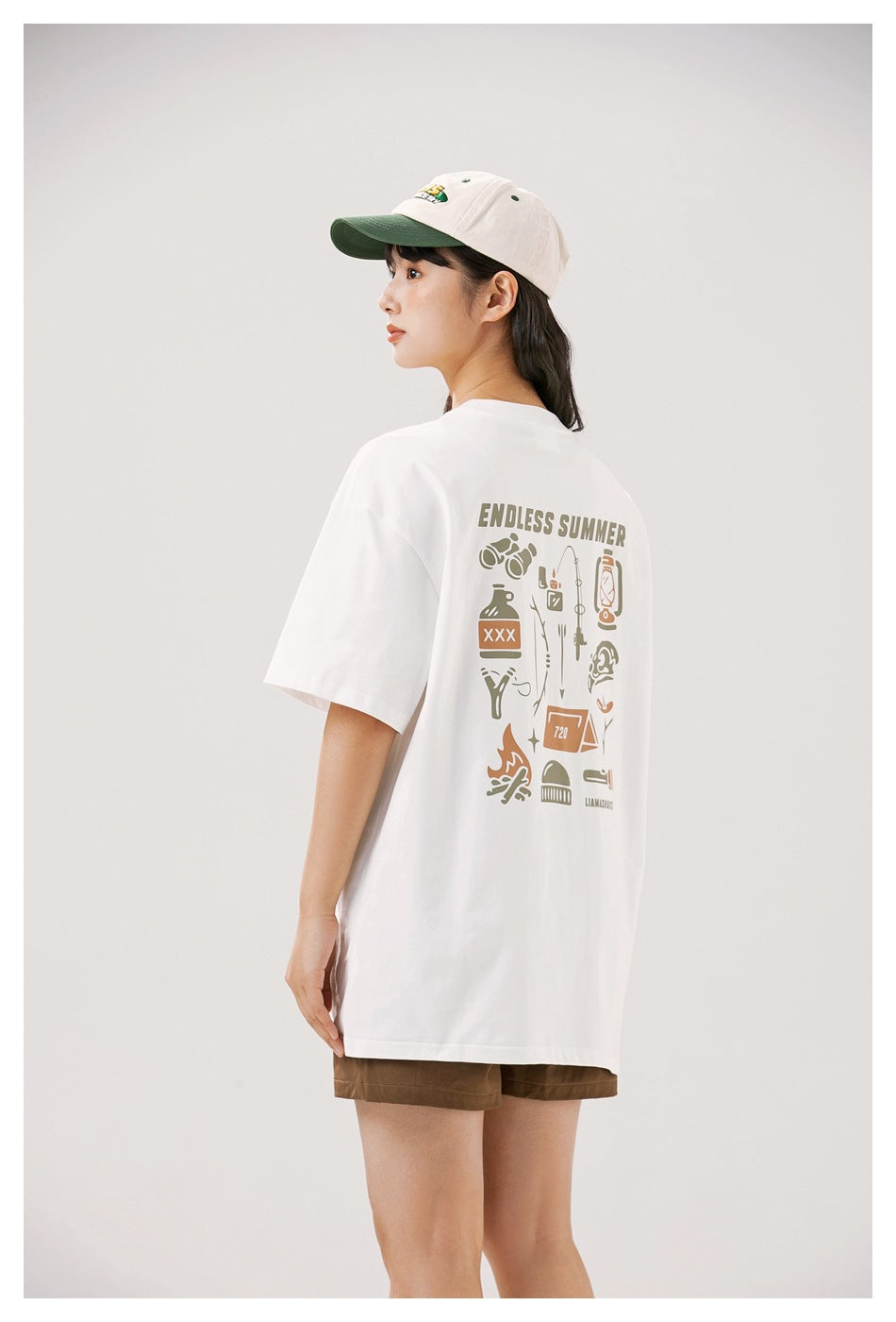 Model showing the back of an oversized white T-shirt with a large camping-themed graphic.