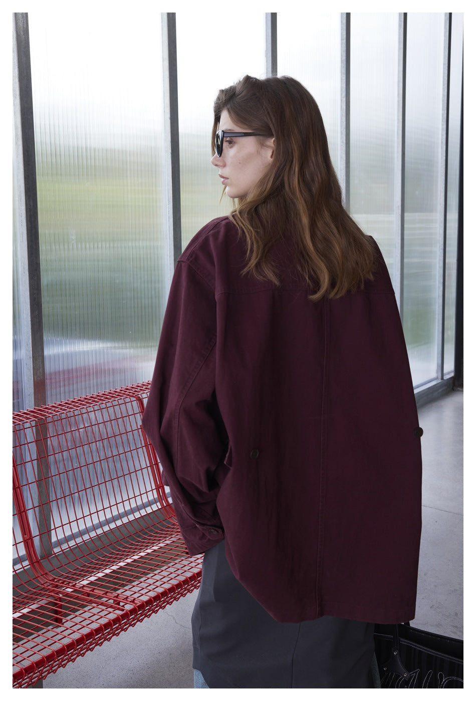 Back view of a model wearing an oversized burgundy jacket with a black collar and buttoned cuffs.
